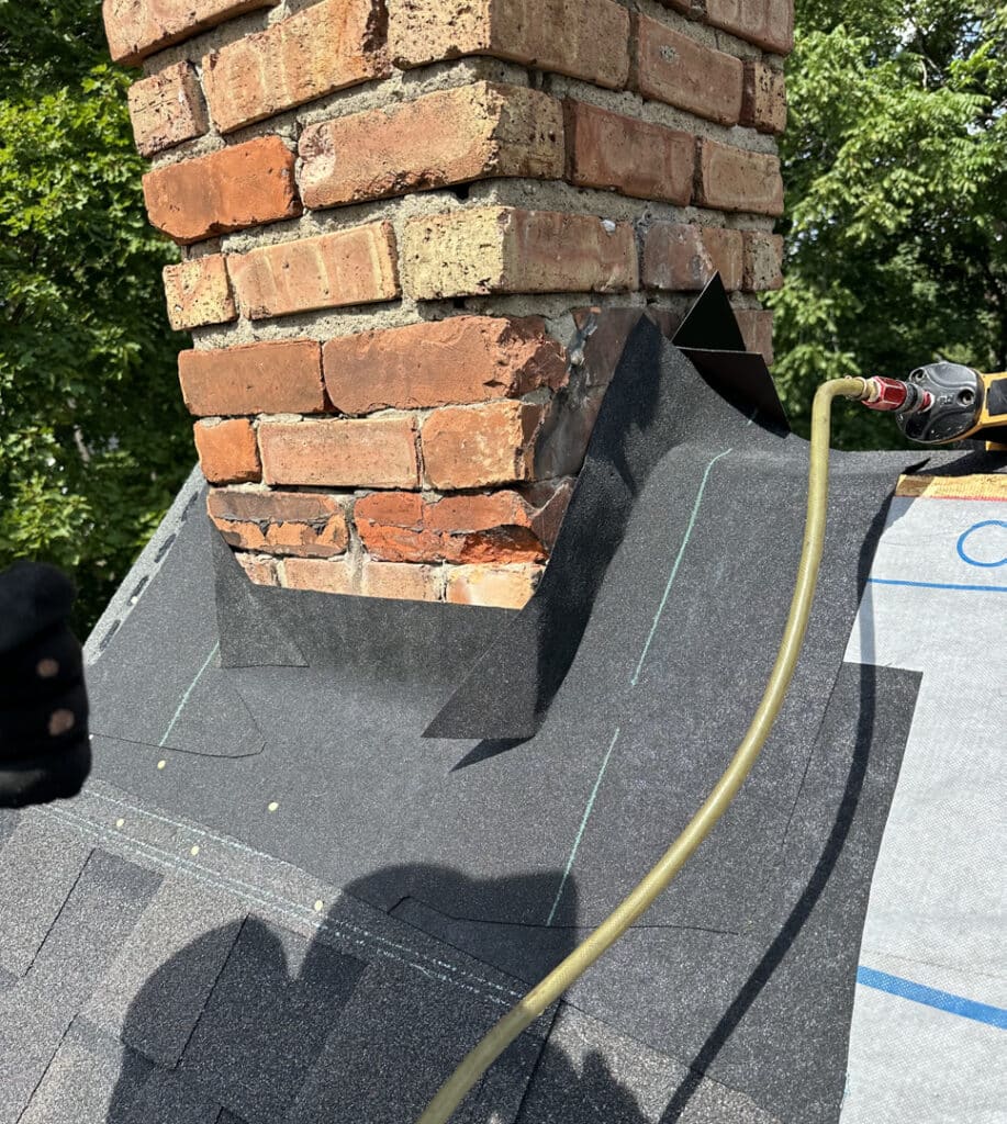 Flashing is installed over base flashing onto chimney and covers the top edge of the base flashing with a high-strength caulking seal.