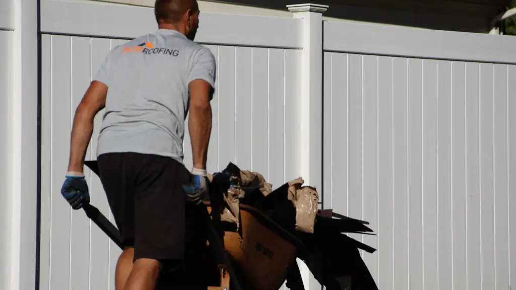 BCM Roofing crew member cleaning up roof debris from the ground around a house
