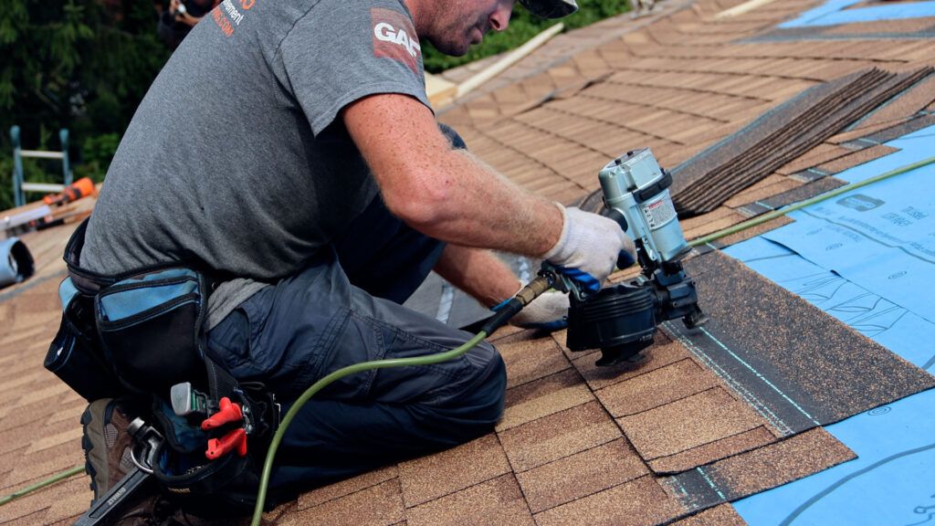 BCM Roofing crew member installing shingles with a nail gun on a home roof, demonstrating how a new roof is installed