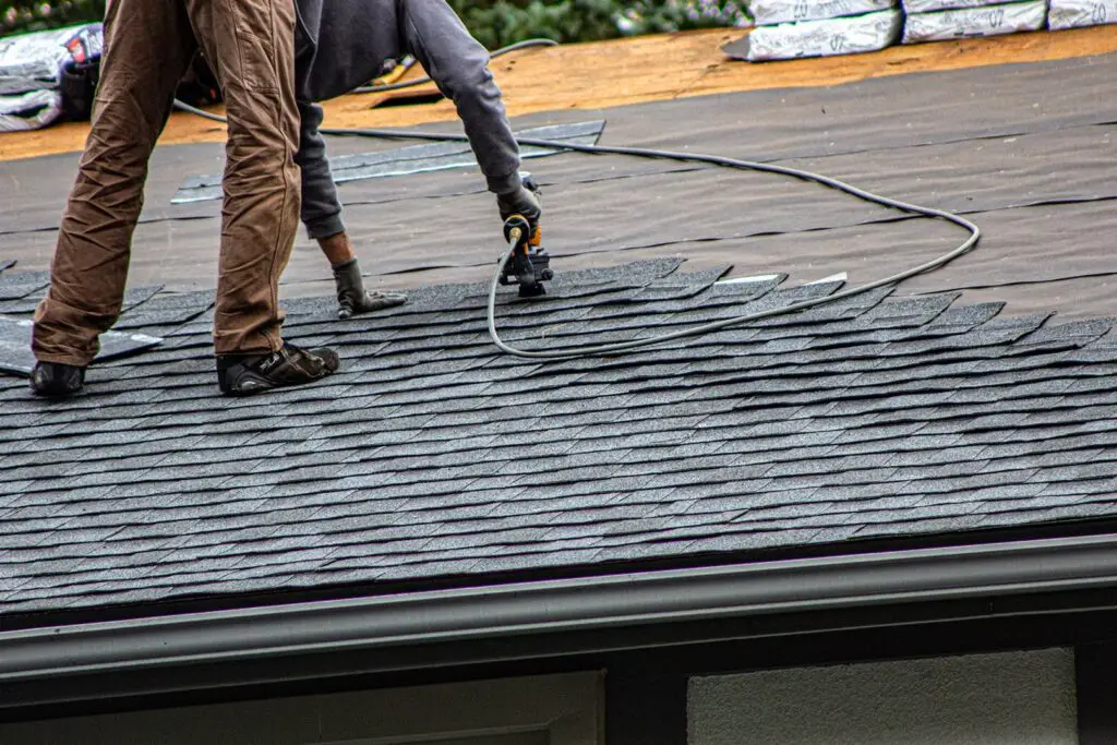 Roofer installing asphalt shingles with a nail gun mid-slope on residential roof.