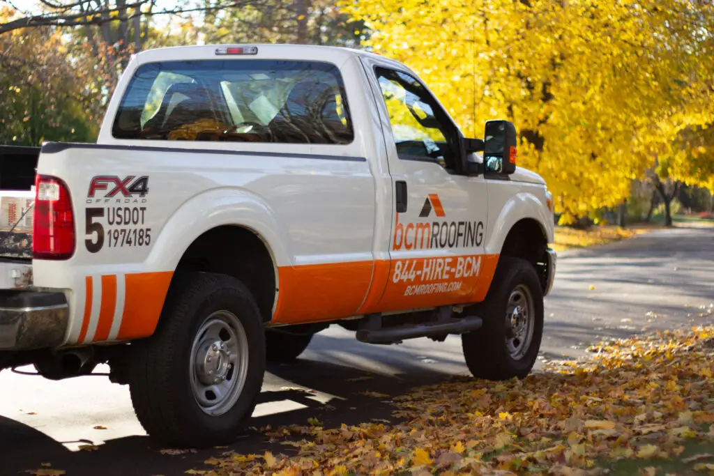 About Us 9 BCM Roofing company truck parked on street during autumn.