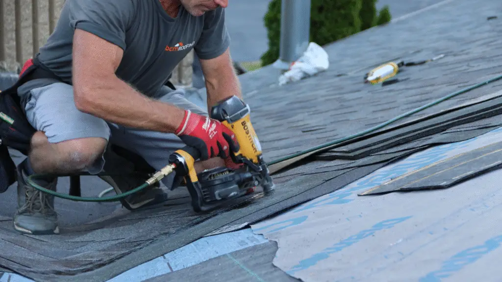 BCM Roofing contractor securing an asphalt shingle near roof valley of commercial roof.