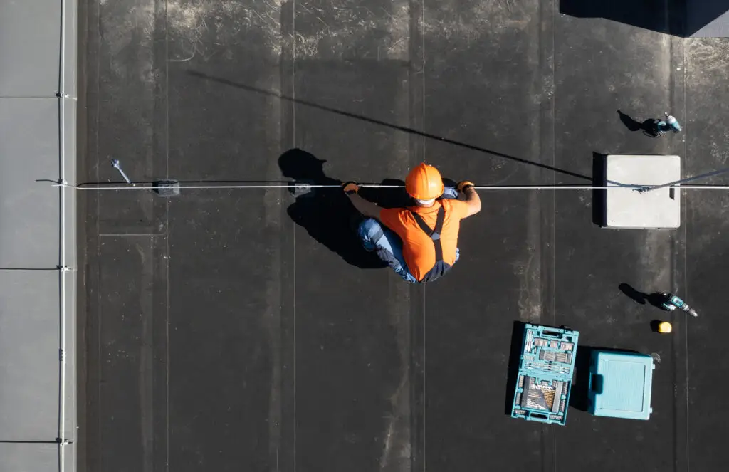 Commercial roofing technician installing a lightning protection system on a flat roof.