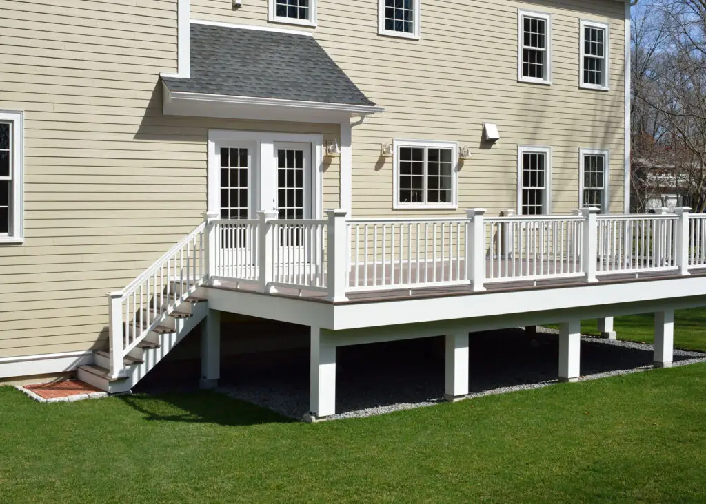 Residential home with beige vinyl siding and raised deck with white railings.