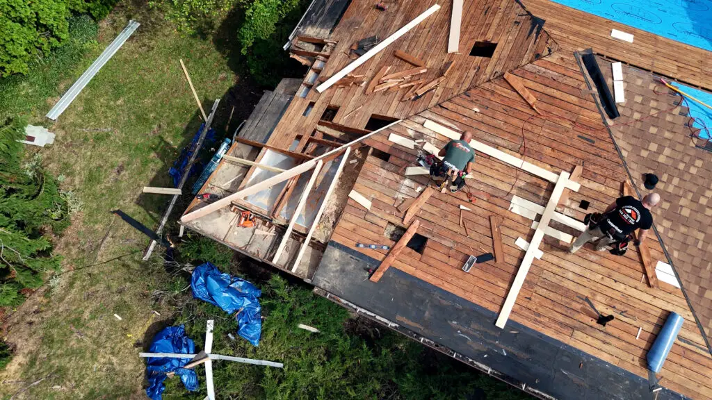 Aerial view of BCM Roofing contractors repairing decking and framing on an exposed roof in Orion, MI.