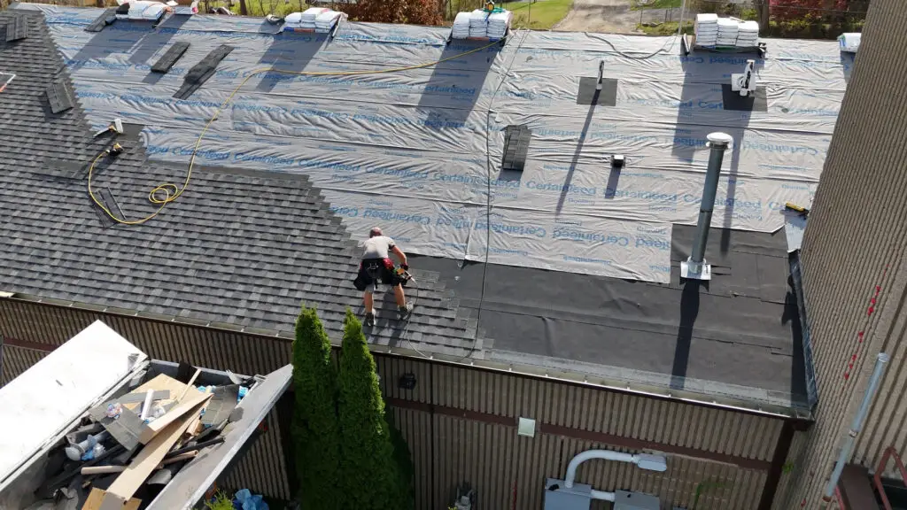Aerial view of roofer installing asphalt shingles on a commercial roof in Royal Oak, MI.