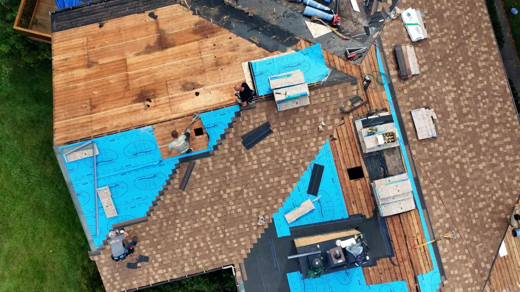 Aerial view of Roofing crew preparing roof for underlayment and installing asphalt shingles in Oxford, MI.