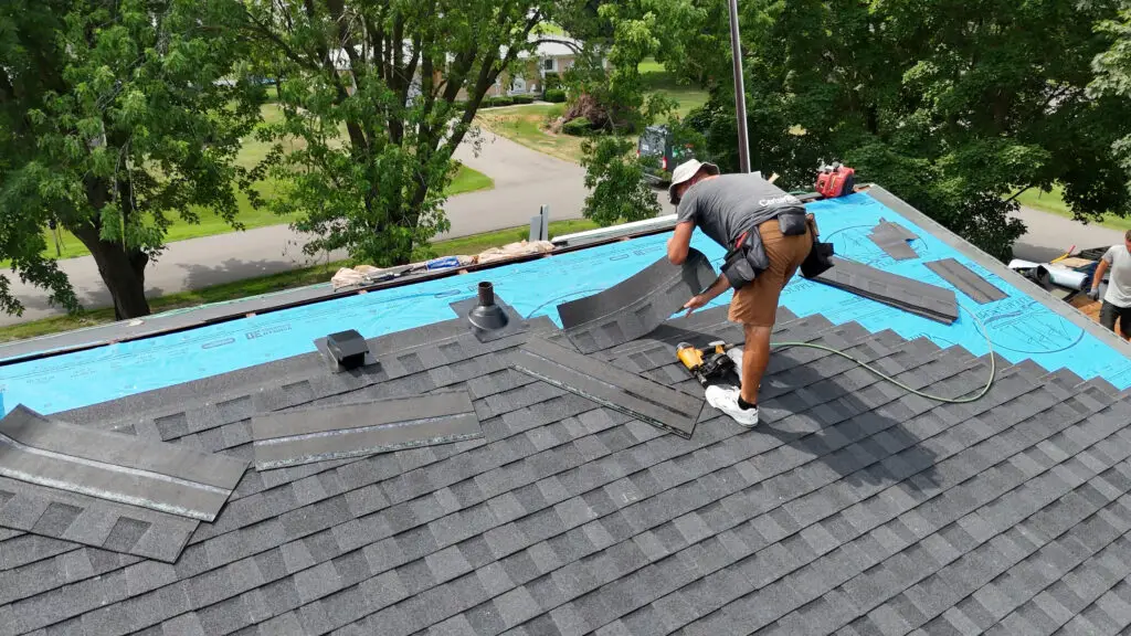 BCM Roofing contractor positioning a shingle course around a pipe boot flashing in Hadley, MI.