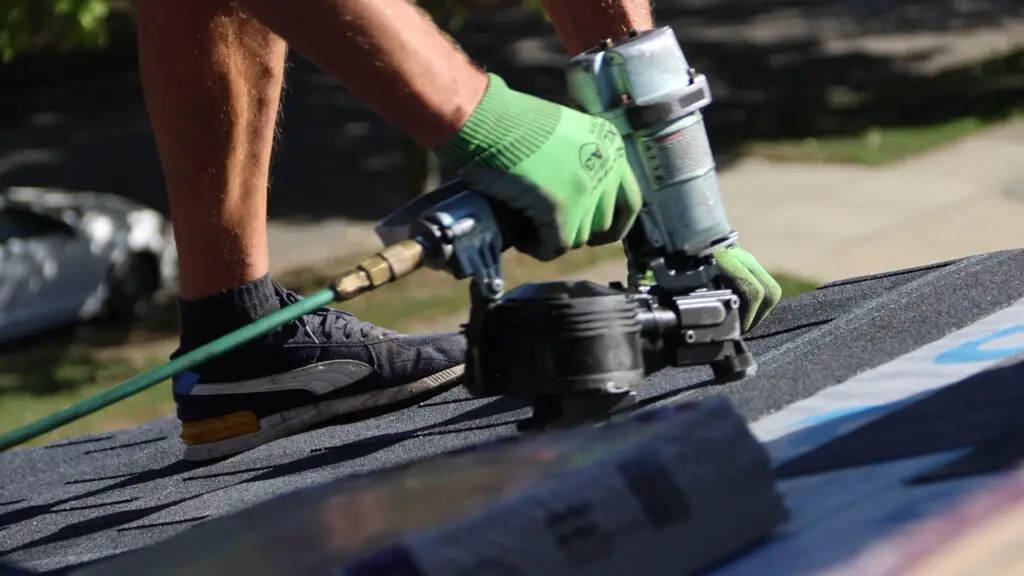 Close-up of roofer installing an asphalt shingle with a nail gun on a residential roof in Village of Clarkston, MI.