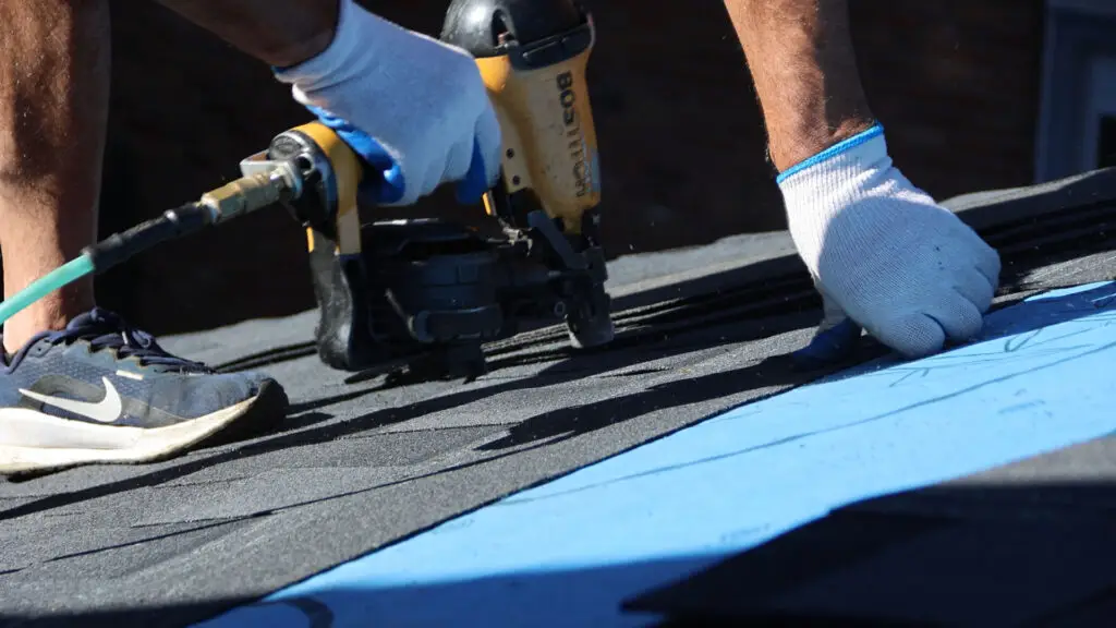 Close-up of roofer securing asphalt shingle during roof replacement in Metamora, MI.