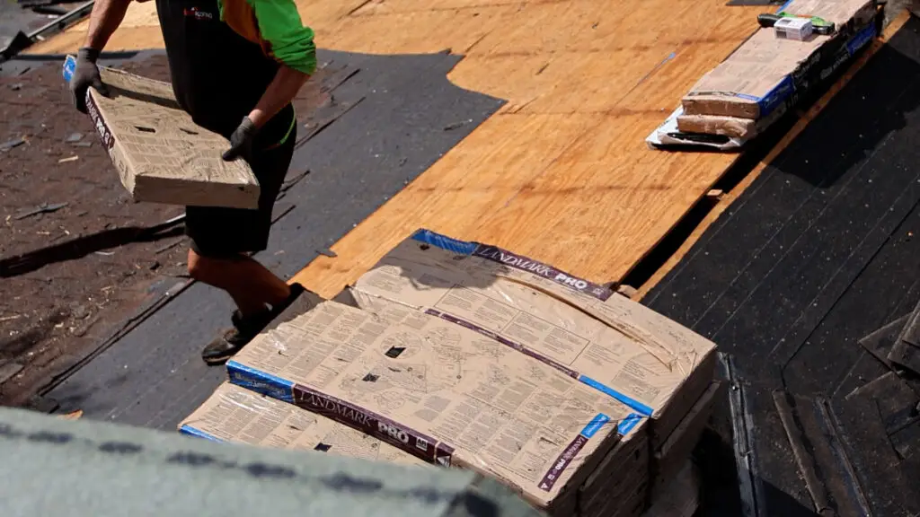 Roofer carrying a bundle of asphalt shingles across exposed roof decking in Madison Heights, MI.