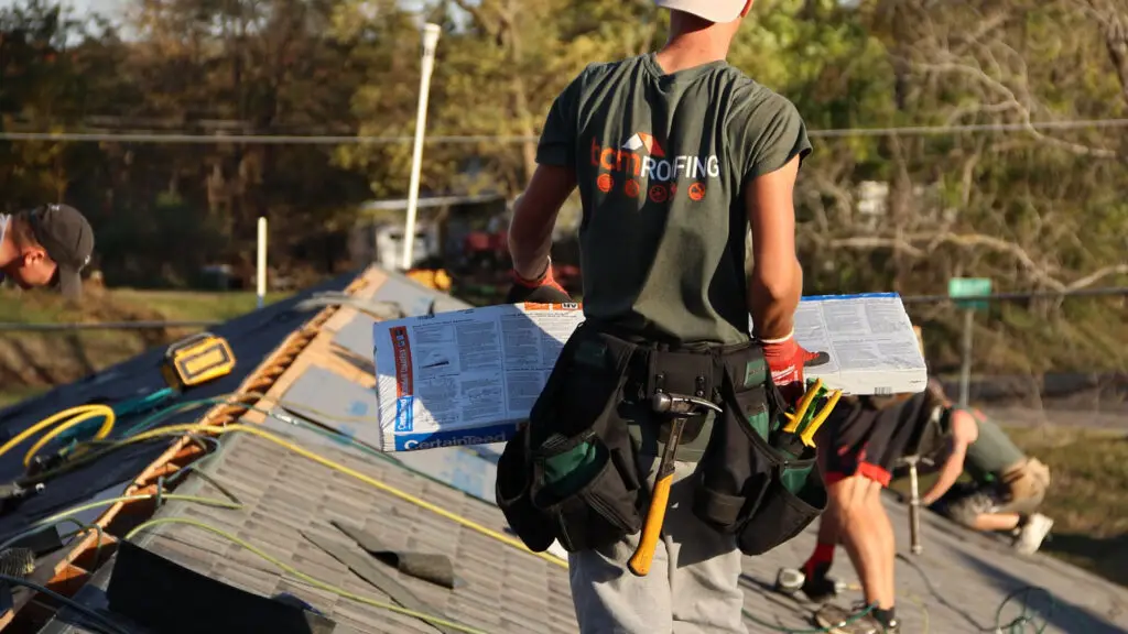 Roofer carrying a bundle of asphalt shingles on a roof in Rochester, MI.