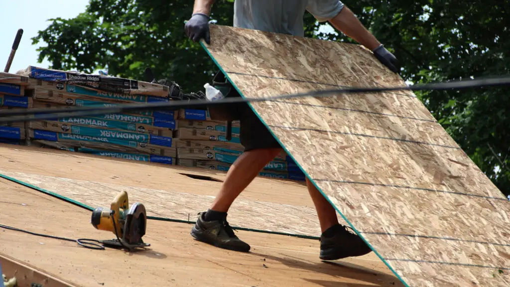 Roofer carrying wood to repair roof decking in Flushing, MI.