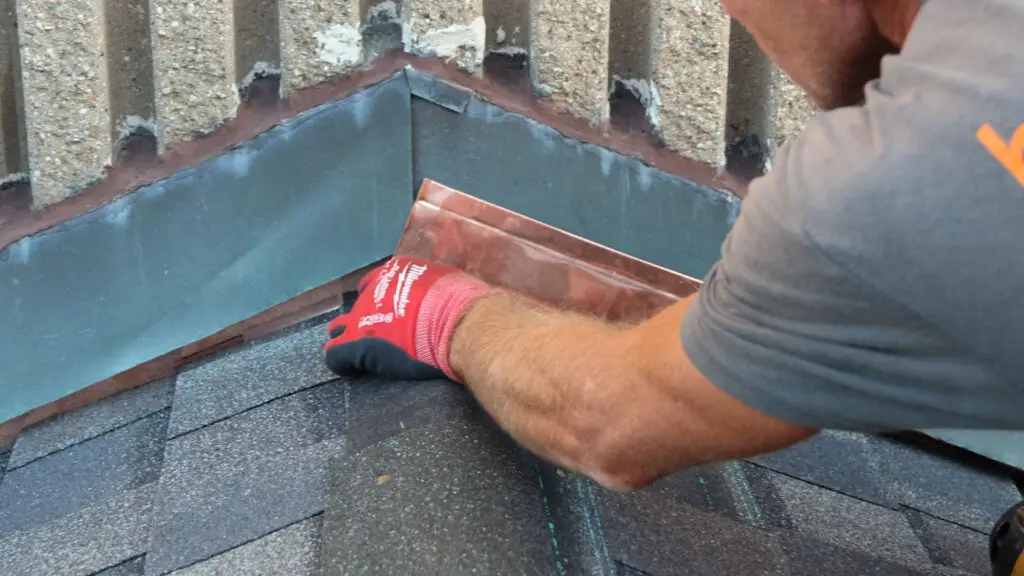Roofer fitting metal flashing at a roof-to-wall intersection in Rochester, MI.