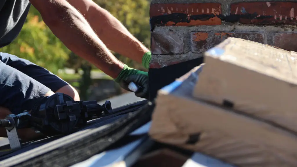 Roofer fitting shingles around chimney step flashing during a roof installation in Mount Morris, MI.