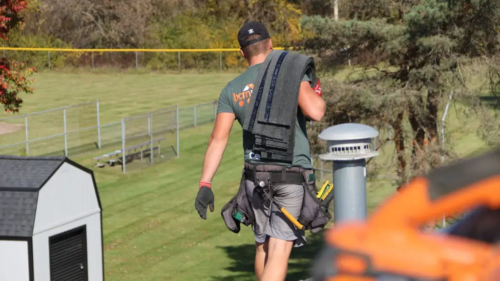 Roofer hauling a bundle of asphalt shingles during a roof replacement in Genesee, MI.