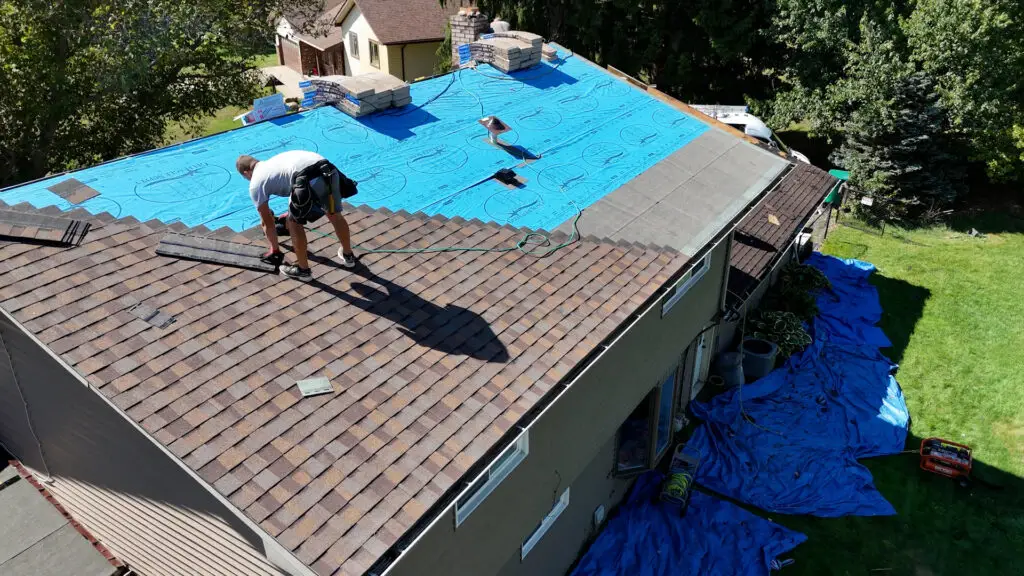 Roofer installing asphalt shingles mid-slope of roof in Mundy, MI.