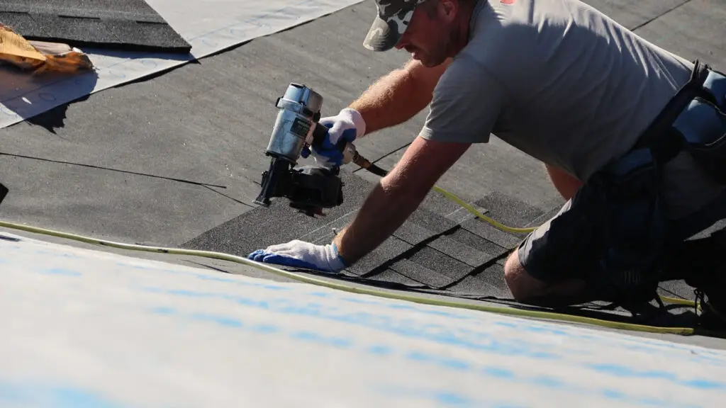 Roofer installing asphalt shingles on roof with nail gun in Beverly Hills, MI.
