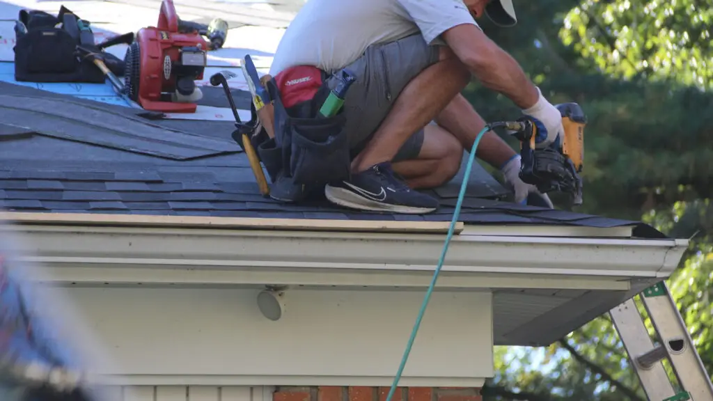 Roofer installing asphalt shingles with a nail gun at the roof eave in White Lake, MI.