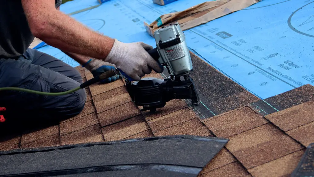 Roofer installing asphalt shingles with a nail gun during a roof replacement in Davison, MI.