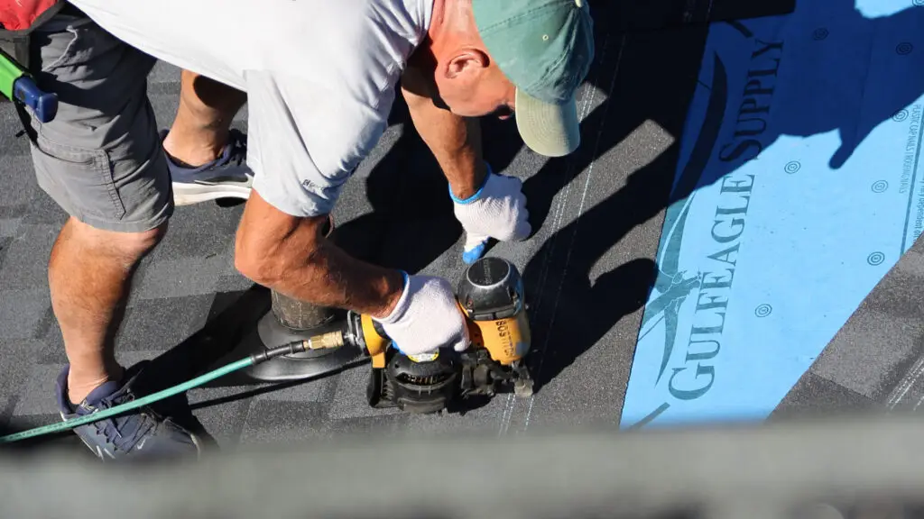 Roofer installing asphalt shingles with a nail gun in Mount Morris, MI.