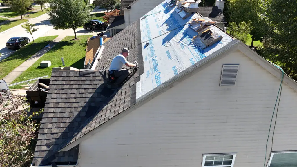 Roofer installing asphalt shingles with a nail gun mid-slope in Genesee, MI.
