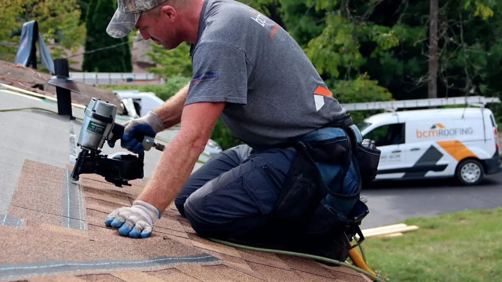 Roofer installing asphalt shingles with a nail gun on a residential roof in Novi, MI.