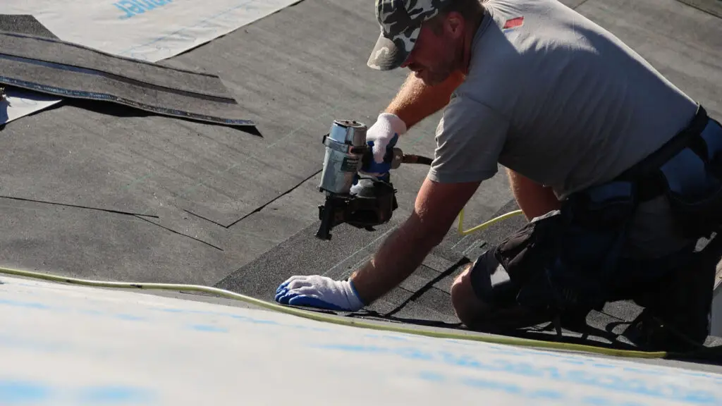 Roofer installing asphalt shingles with nail gun over underlayment in Milford, MI.