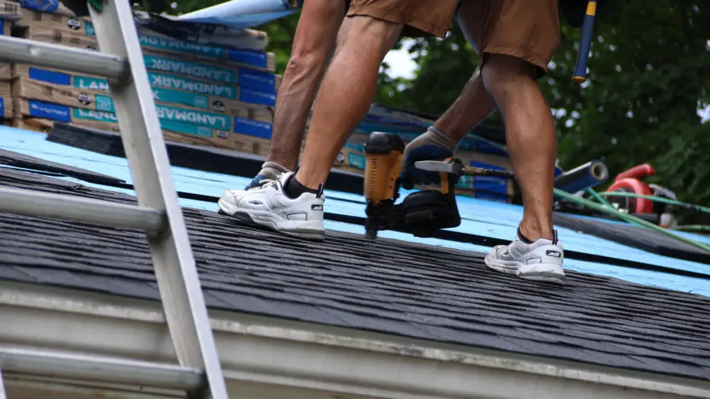 Roofer installing shingles with a nail gun during roof replacement in Walled Lake, MI.
