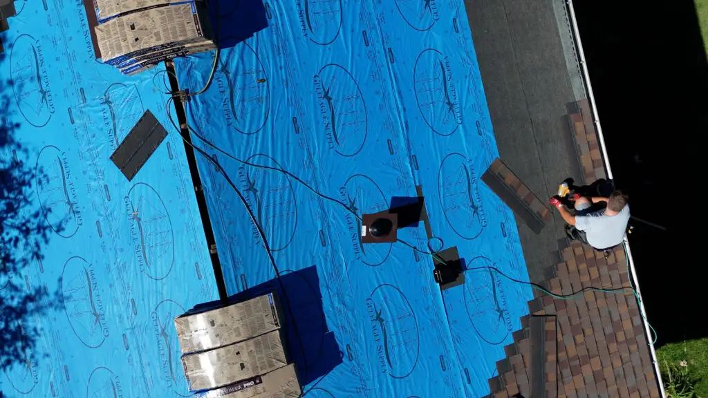 Roofer installing starter course of asphalt shingles at roof eave in Mayfield, MI.