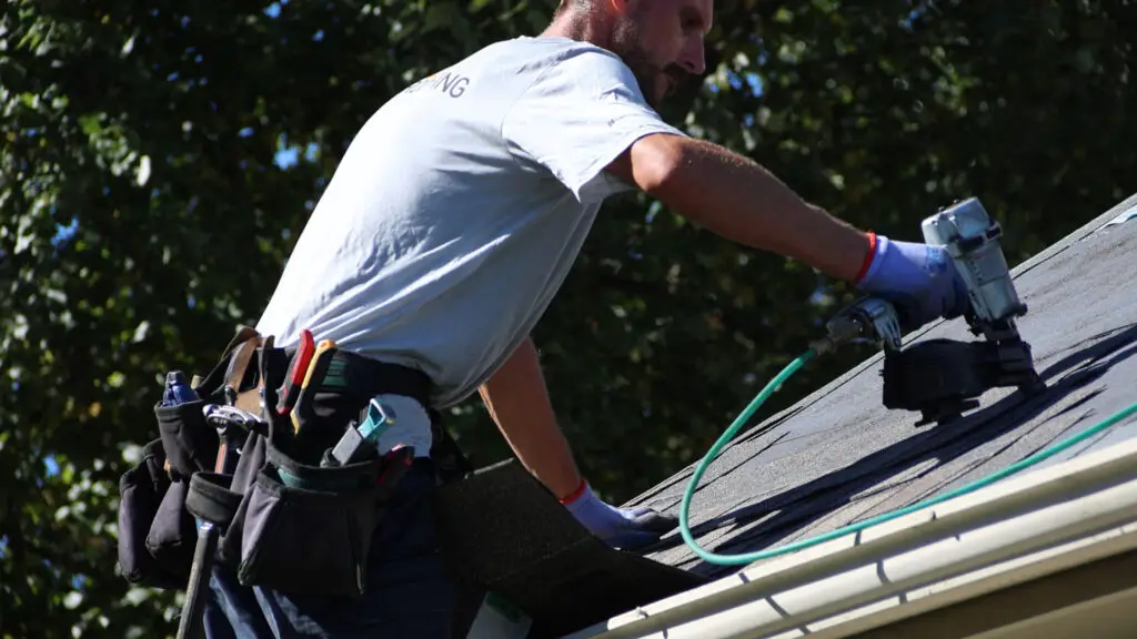 Roofer installing the starter course of asphalt shingles with a nail gun at the roof eave in Burlington, MI.