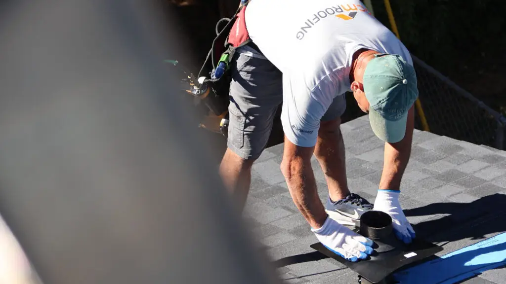 Roofer installing vent pipe flashing on asphalt shingle roof in Beverly Hills, MI.
