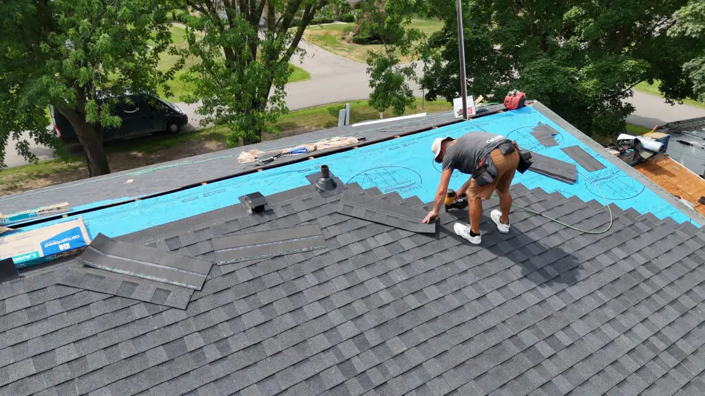 Roofer installs asphalt shingles with nail gun during roof replacement in White Lake, MI.