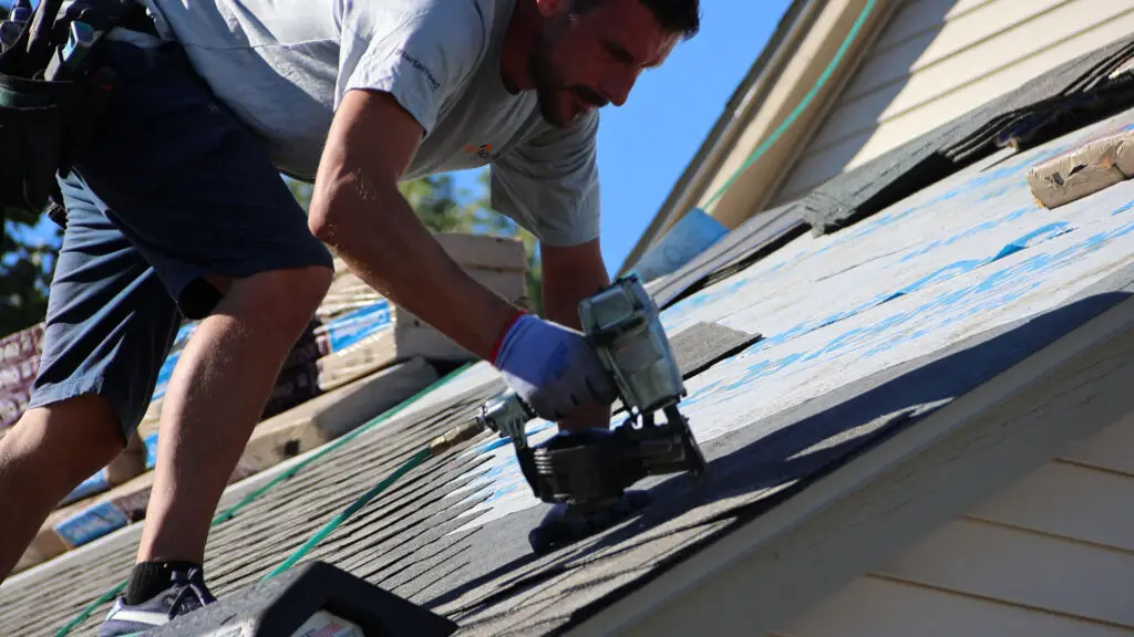 Roofer nailing asphalt shingles to residential roof in Bloomfield, MI.
