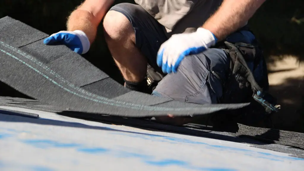 Roofer placing asphalt shingle on underlayment during roof replacement in Village of Clarkston, MI.