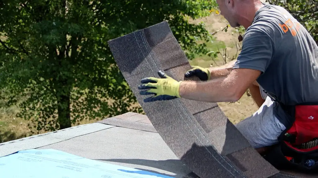 Roofer positioning an asphalt shingle for installation near the roof eave in Madison Heights, MI.
