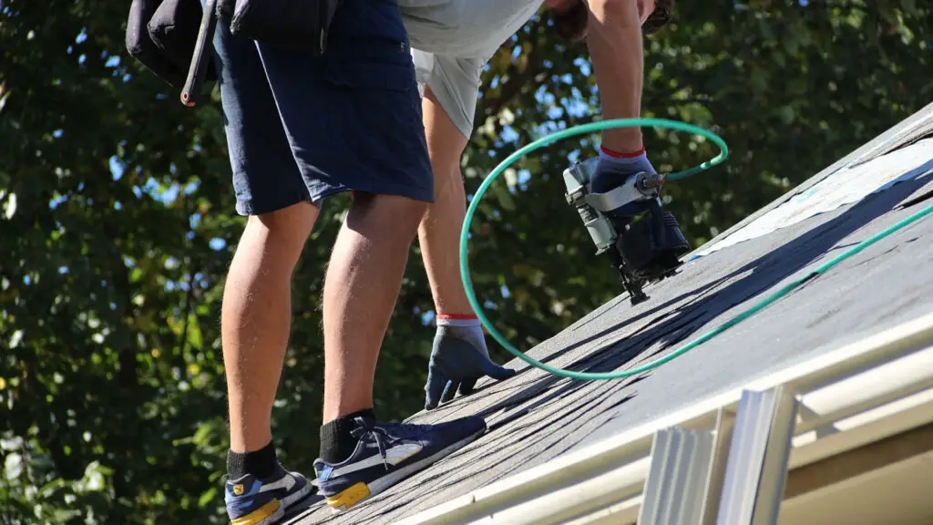 Roofer positioning an asphalt shingle on a steep-slope roof in Independence, MI.