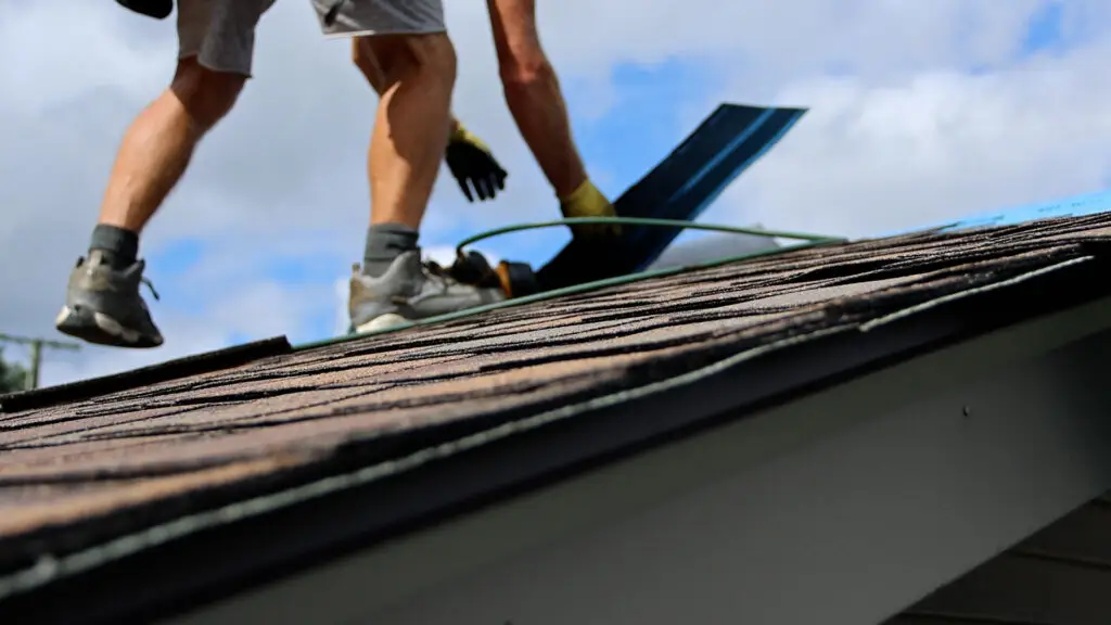 Roofer positioning asphalt shingle during roof replacement in Mayfield, MI.