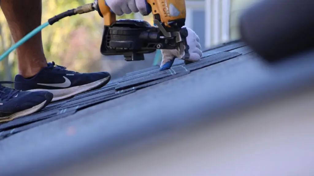 Roofer positioning asphalt shingles during roof replacement project in Holly, MI.