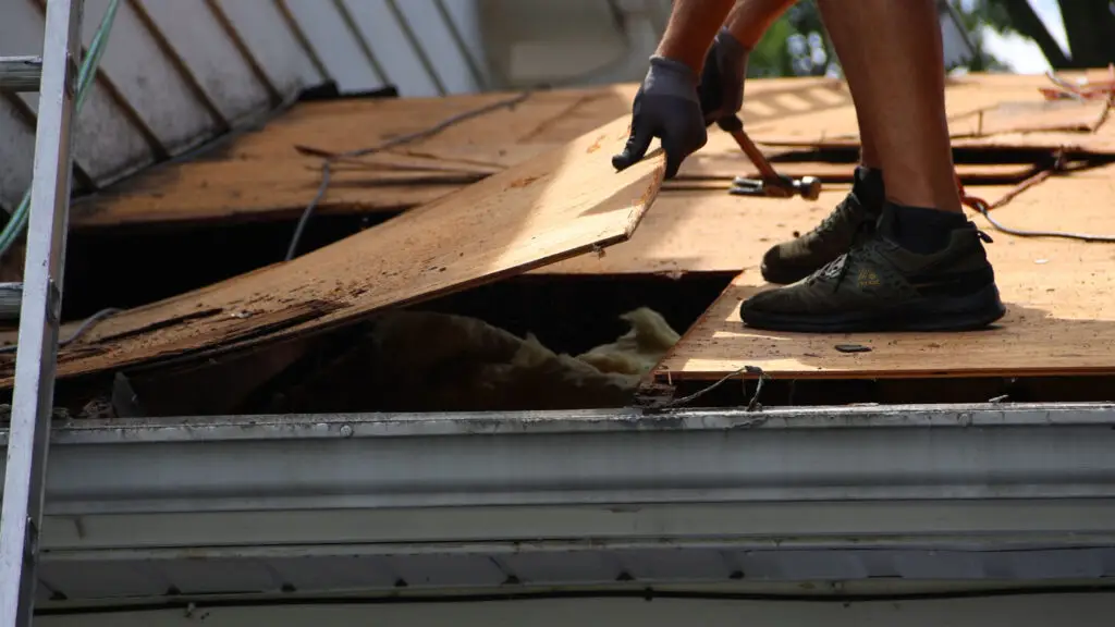 Roofer removing damaged roof decking during a repair in Wolverine Lake, MI.