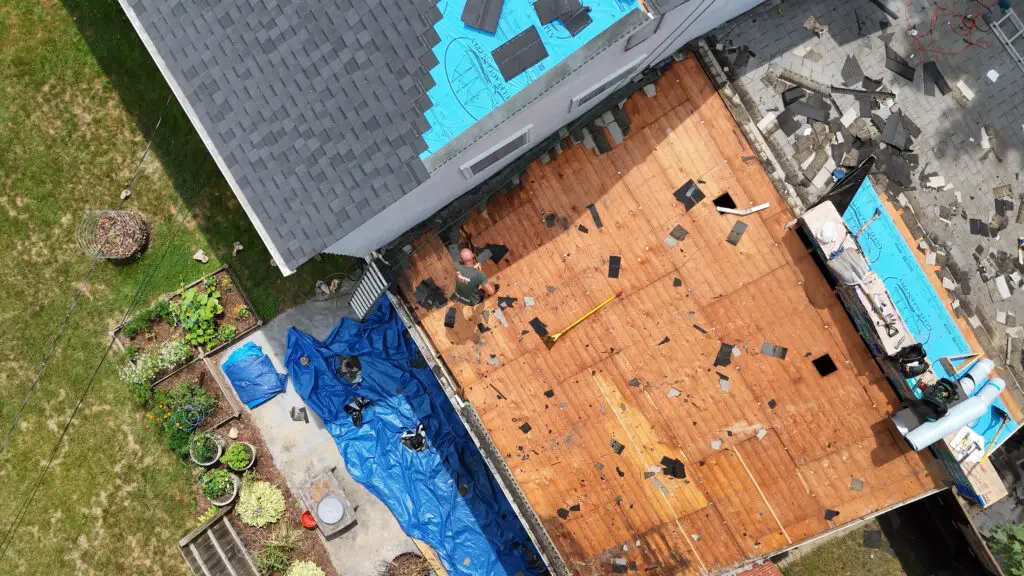 Roofer removing old asphalt shingles and flashing during a residential roof replacement in Walled Lake, MI.