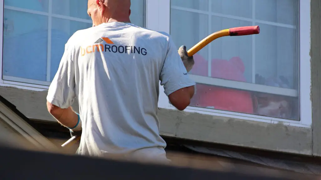 Roofer removing old asphalt shingles from residential roof in Burlington, MI.