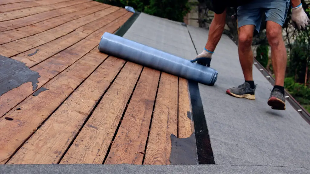 Roofer rolling underlayment over the exposed roof deck in Orion, MI.
