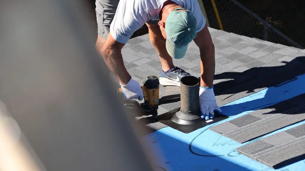 Roofer securing a pipe boot flashing with a nail gun in Vienna, MI.