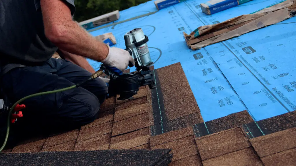 Roofer securing an asphalt shingle with a nail gun during roof replacement in Clarkston, MI.