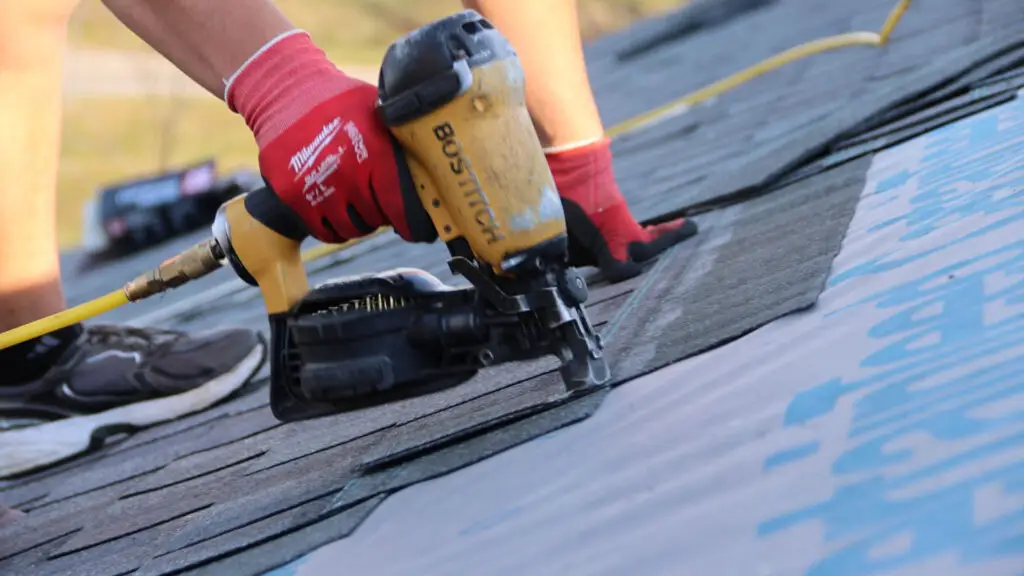 Roofer securing asphalt shingles to roof with nail gun in Dryden, MI.