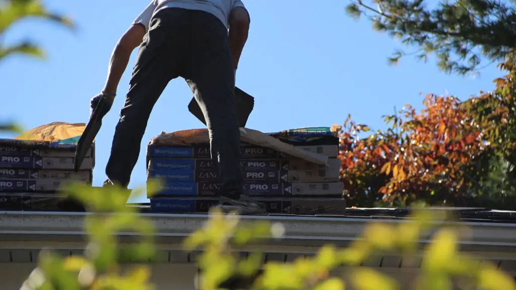 Roofer staging shingle bundles at the roof eave in Holly, MI.