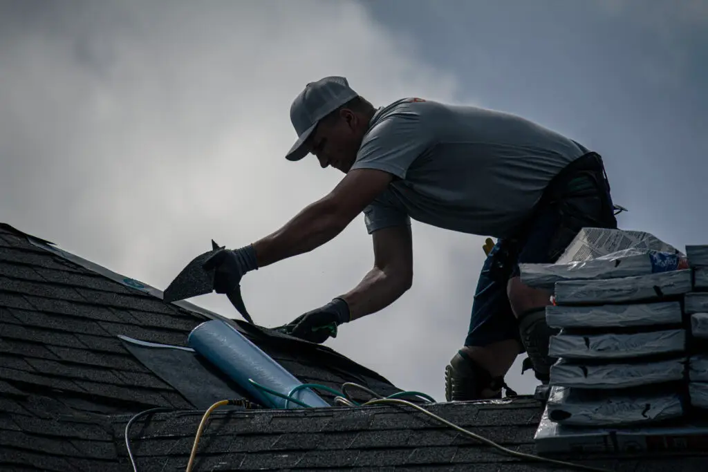 Roofer trimming an asphalt shingle with a utility knife at the roof edge in Oregon, MI.