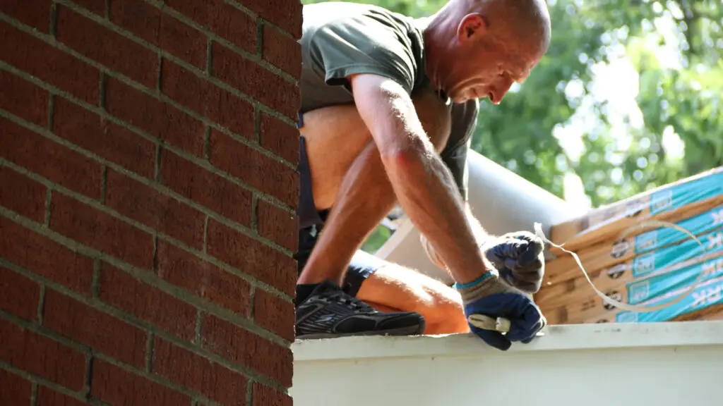 Roofer trimming material with snips at the roof eave in Huntington Woods, MI.