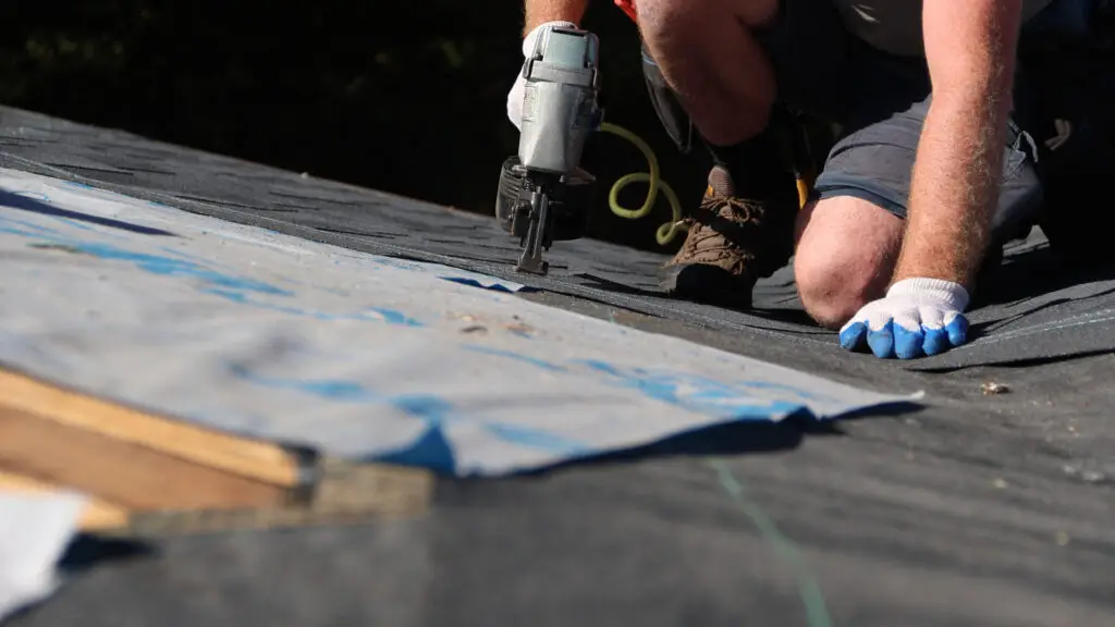 Roofer using a nail gun to install asphalt shingles along a roof valley during roof replacement in Imlay City, MI.